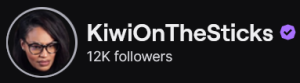 KiwiIOnTheSticks' Twitch logo and follower count (12k). Logo is a picture of a black woman with pressed dark brown hair wearing black framed glasses, against a black background. Image links to KiwiOnTheSticks' Twitch page.
