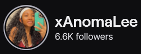 XAnomaLee's Twitch logo and follower count (6.6k). Logo is a picture of a smiling black woman with long curly hair, wearing a white headband and a red top. She is holding up her phone taking a mirror selfie. Image links to XAnomaLee's Twitch page.